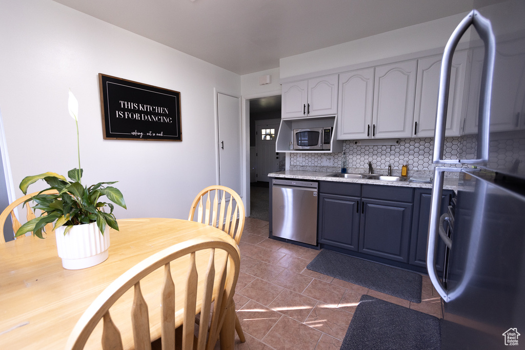 Kitchen featuring dark tile patterned floors, sink, stainless steel appliances, and tasteful backsplash