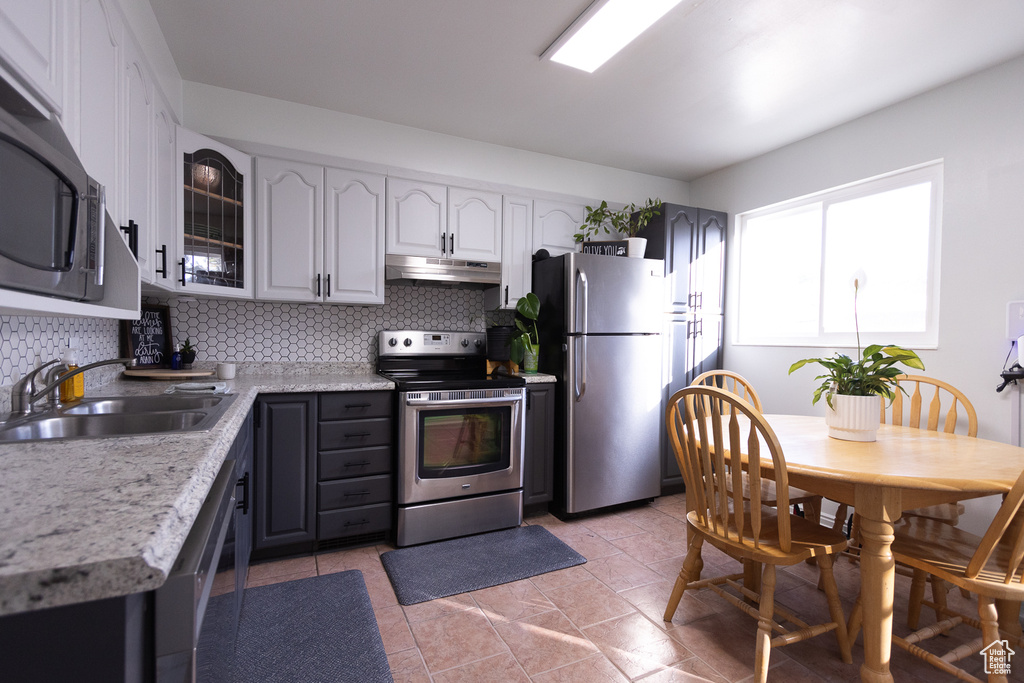 Kitchen featuring gray cabinetry, backsplash, sink, appliances with stainless steel finishes, and light stone counters