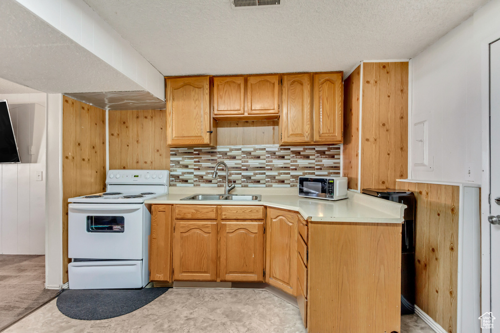 Kitchen featuring decorative backsplash, a textured ceiling, wood walls, sink, and white appliances