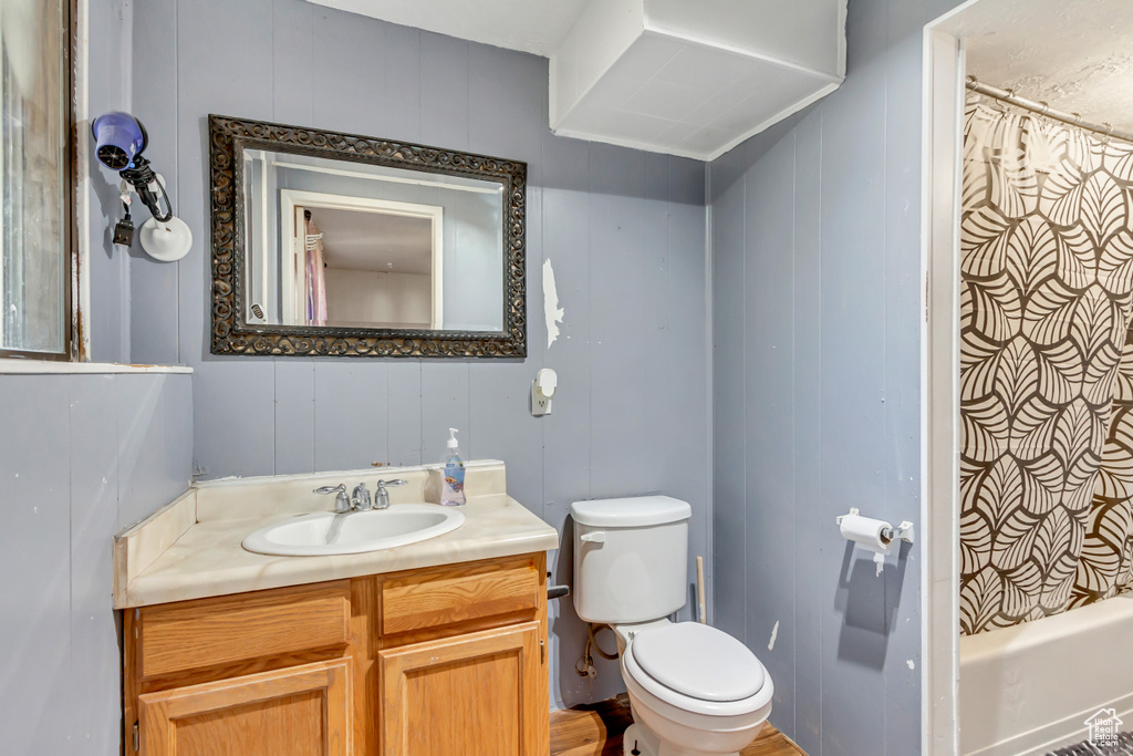 Full bathroom featuring vanity, wooden walls, shower / bath combo, and toilet