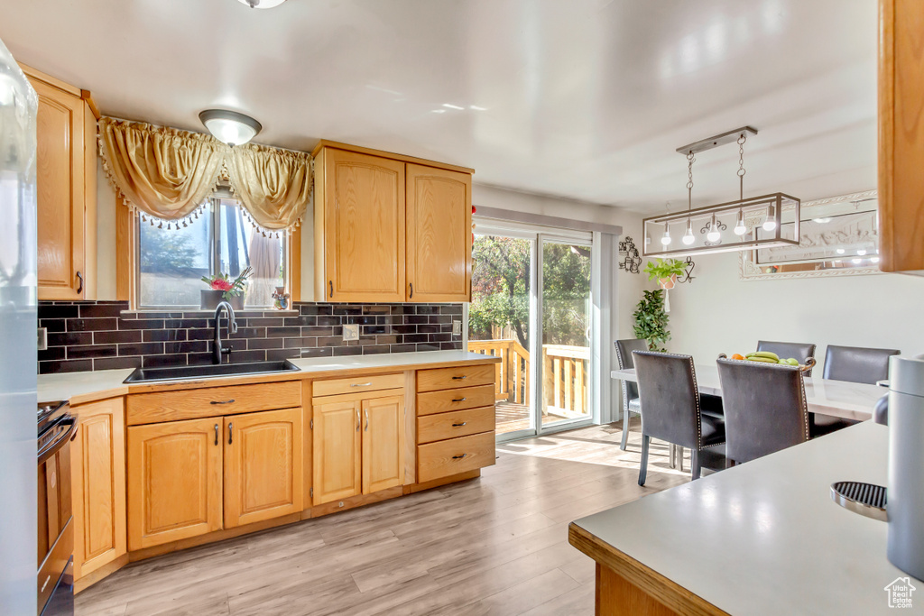 Kitchen featuring sink, light wood-type flooring, range, pendant lighting, and decorative backsplash