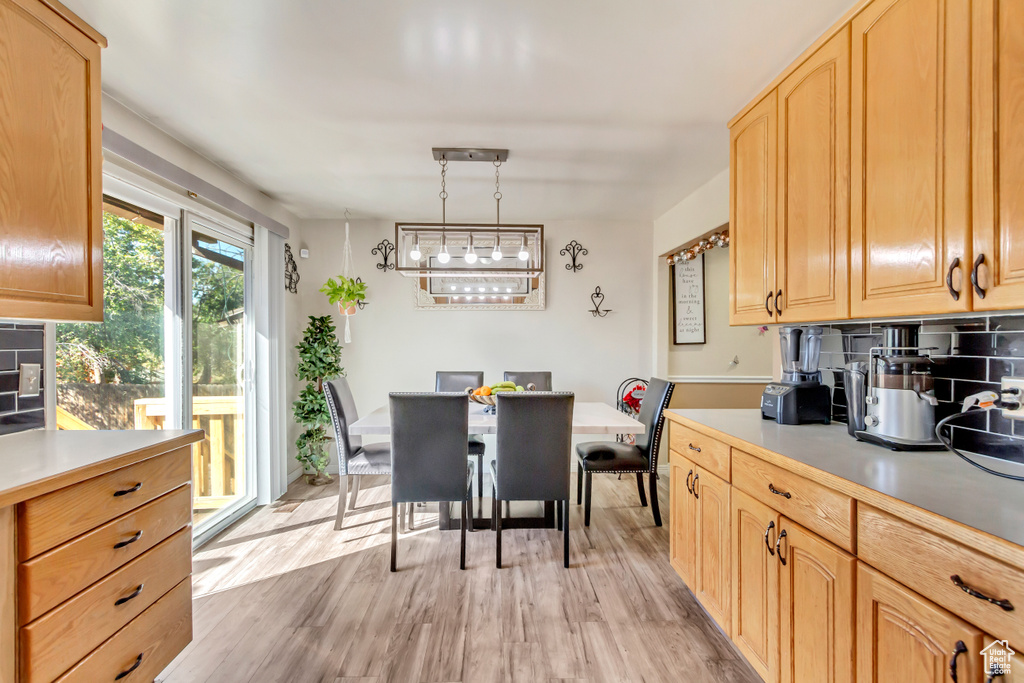 Kitchen featuring light brown cabinetry, decorative backsplash, hanging light fixtures, and light wood-type flooring