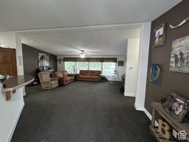 Living room with lofted ceiling, dark colored carpet, and ceiling fan