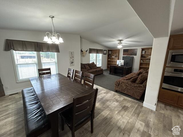 Dining area with wood-type flooring, vaulted ceiling, and ceiling fan with notable chandelier