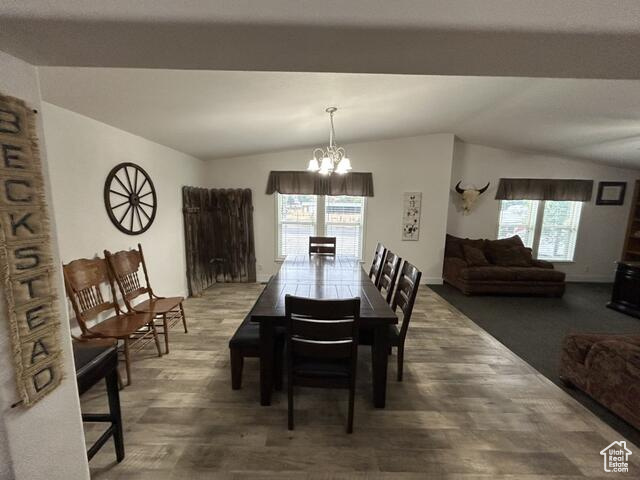 Dining area featuring an inviting chandelier, vaulted ceiling, a healthy amount of sunlight, and dark hardwood / wood-style flooring