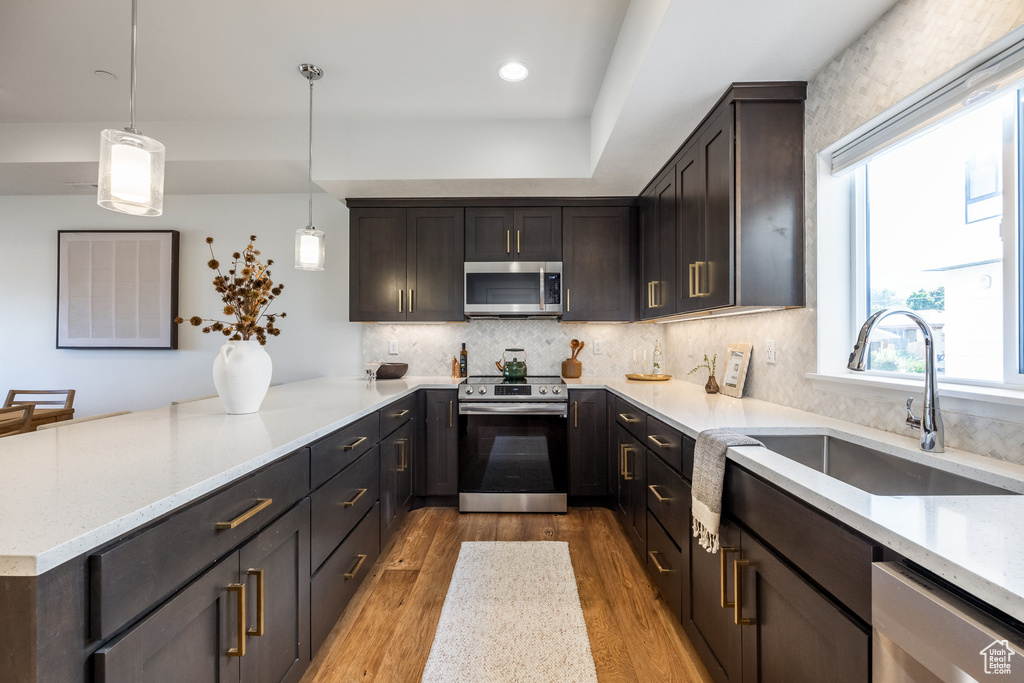 Kitchen featuring light stone counters, appliances with stainless steel finishes, light hardwood / wood-style flooring, pendant lighting, and sink