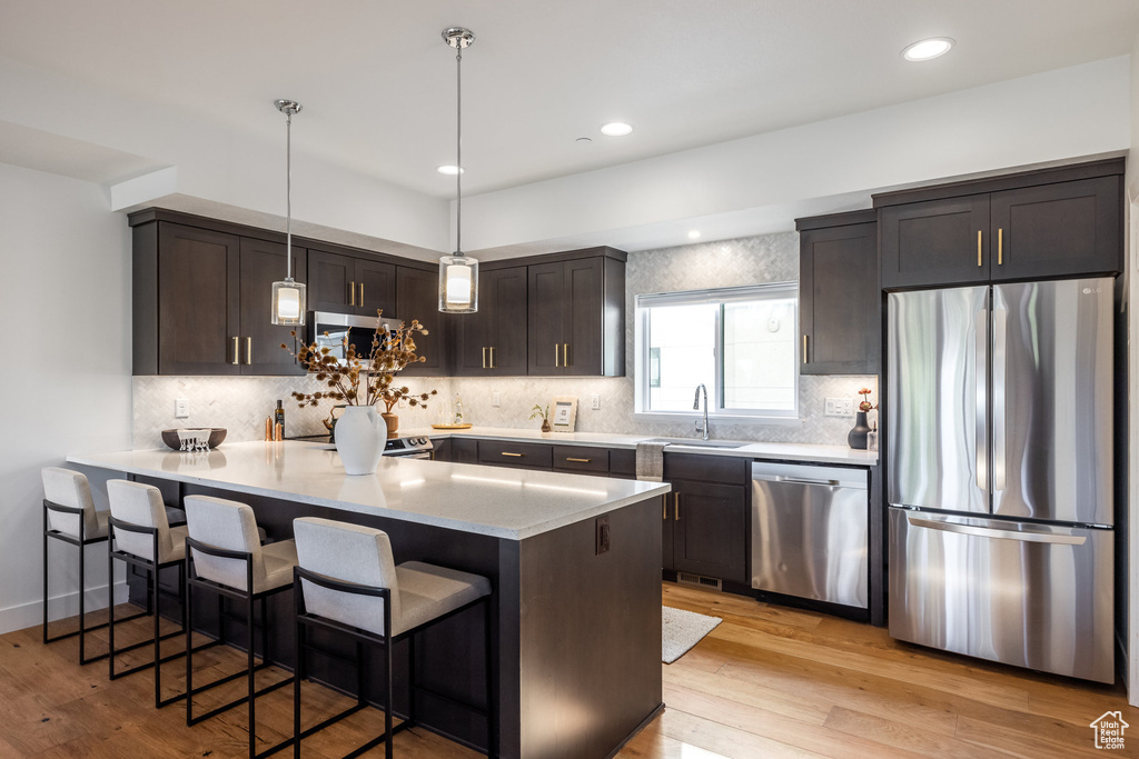 Kitchen with dark brown cabinets, sink, decorative light fixtures, light wood-type flooring, and appliances with stainless steel finishes