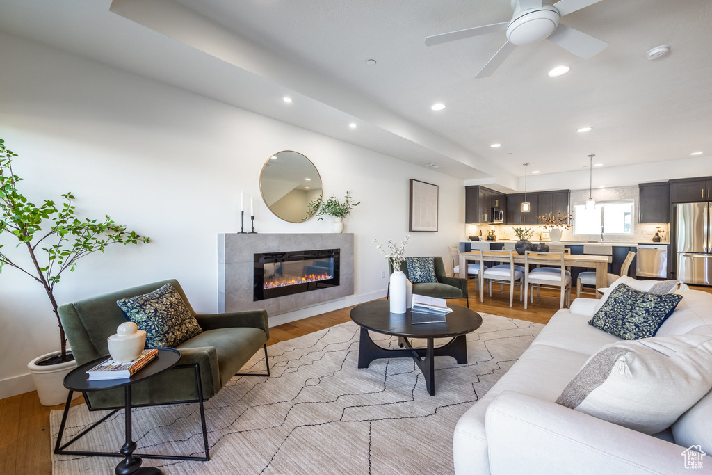 Living room with a fireplace, light wood-type flooring, and ceiling fan