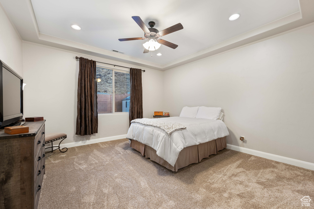 Bedroom featuring light carpet, a tray ceiling, and ceiling fan