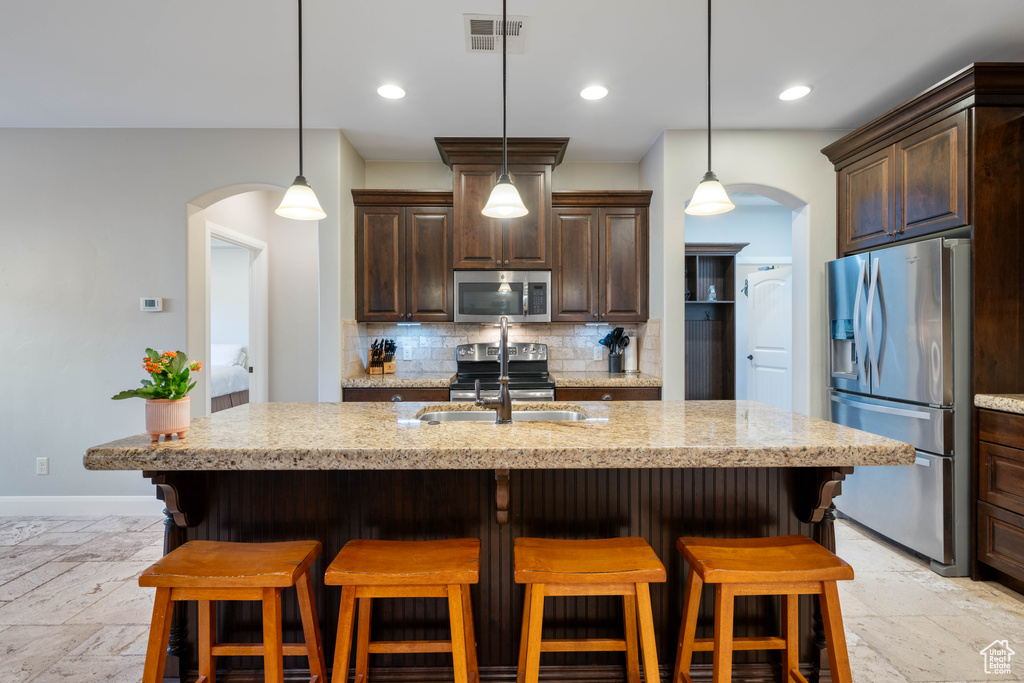 Kitchen featuring an island with sink, stainless steel appliances, dark brown cabinets, sink, and a kitchen bar