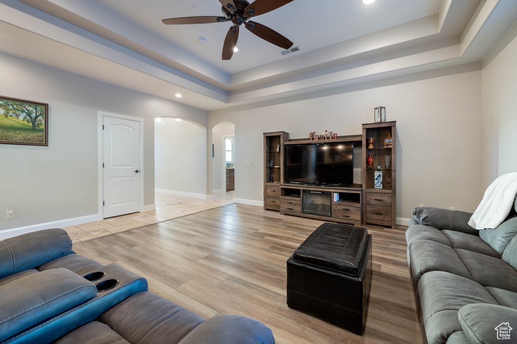 Living room with ceiling fan, a raised ceiling, and light hardwood / wood-style flooring