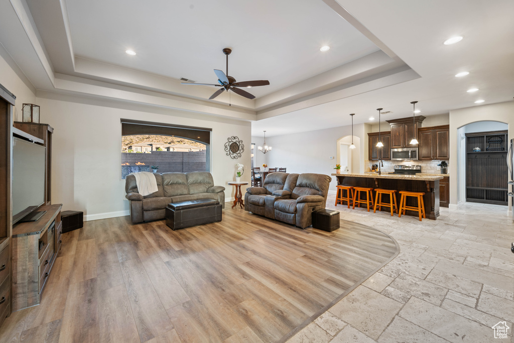 Living room with light hardwood / wood-style flooring, ceiling fan with notable chandelier, and a raised ceiling