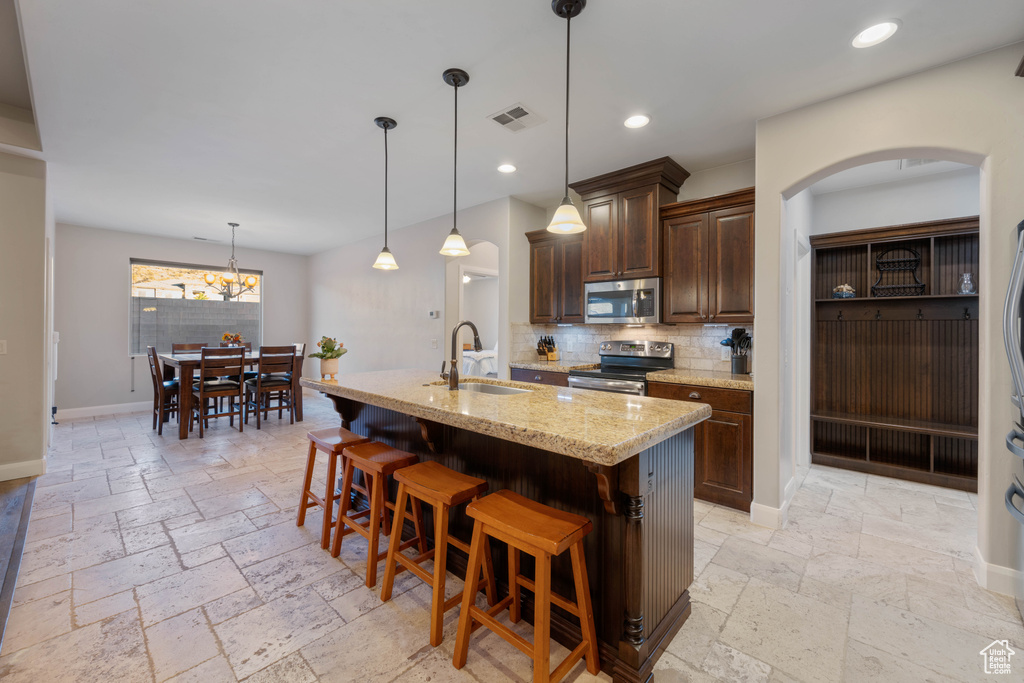 Kitchen with tasteful backsplash, sink, stainless steel appliances, light stone counters, and a center island with sink