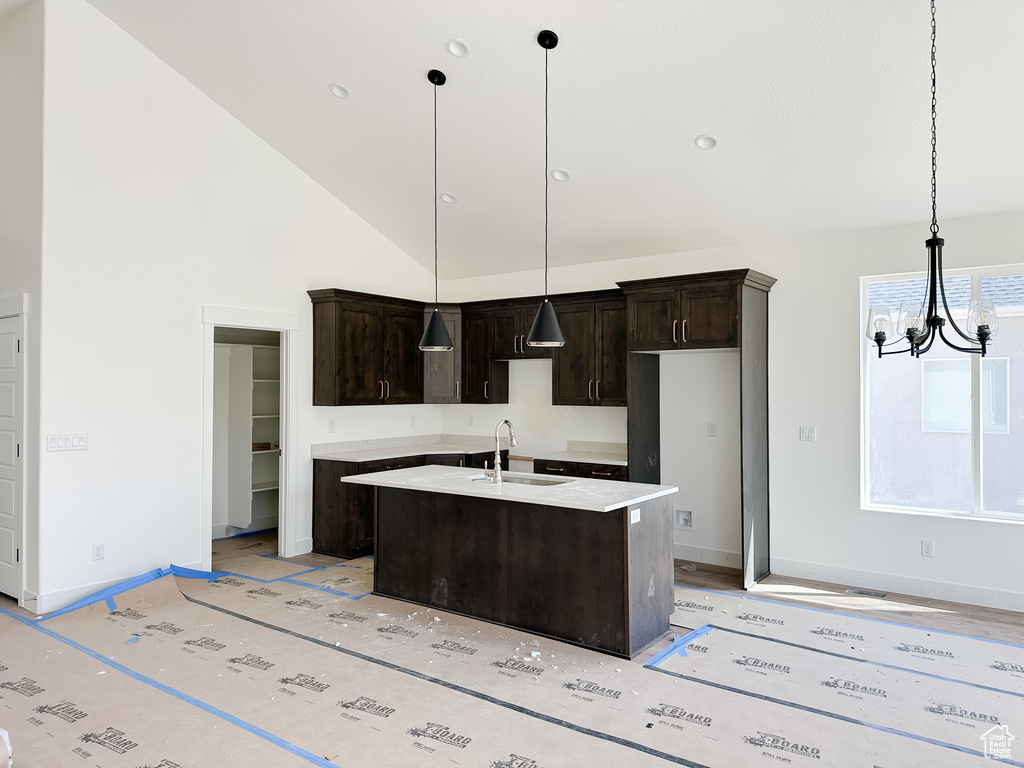 Kitchen featuring an inviting chandelier, dark brown cabinets, a kitchen island with sink, high vaulted ceiling, and a sink