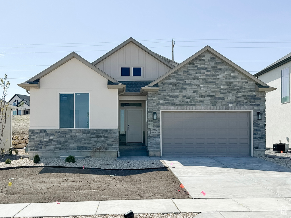 Craftsman inspired home with board and batten siding, a garage, central air condition unit, stone siding, and driveway