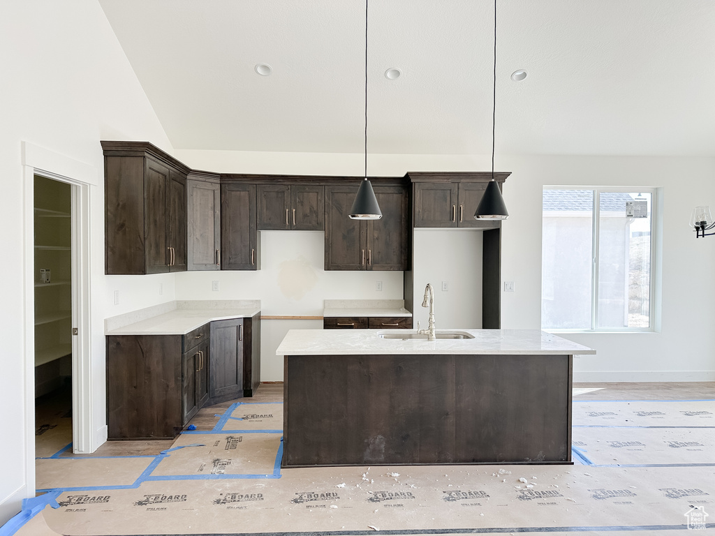 Kitchen with pendant lighting, an island with sink, dark brown cabinetry, a sink, and lofted ceiling