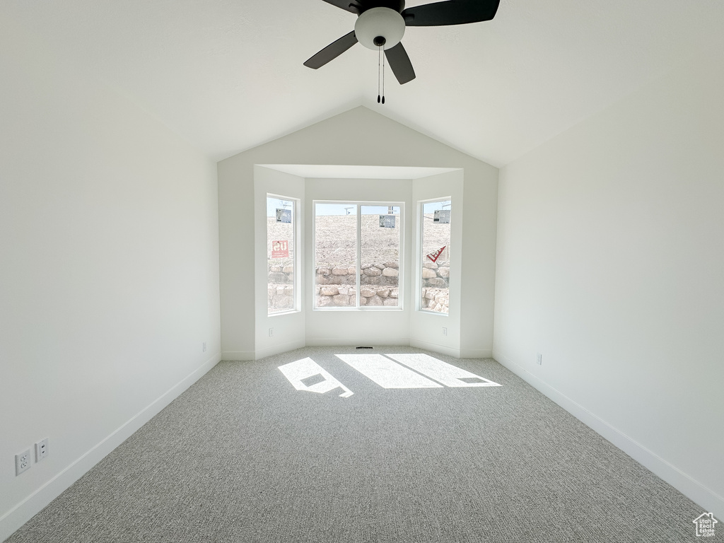 Carpeted empty room featuring baseboards, a ceiling fan, and lofted ceiling