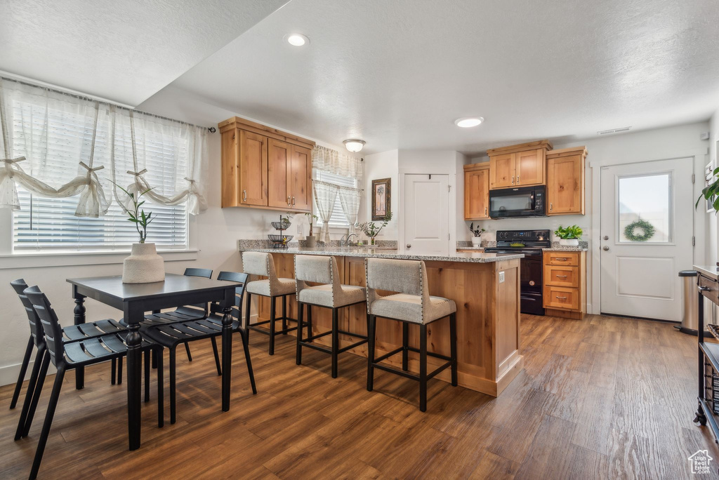 Kitchen featuring light stone countertops, black appliances, a kitchen bar, a textured ceiling, and dark wood-type flooring