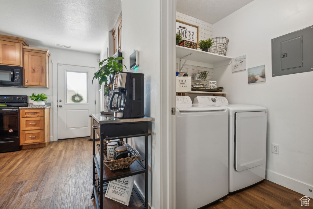 Laundry room with a textured ceiling, electric panel, washer and clothes dryer, and dark hardwood / wood-style flooring