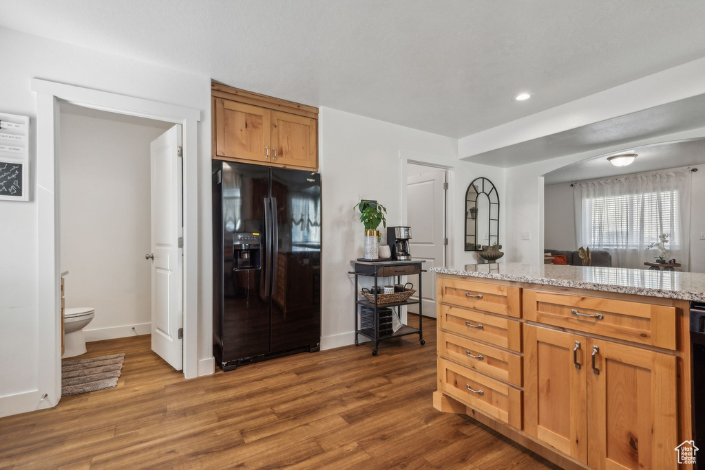 Kitchen with light stone counters, black refrigerator with ice dispenser, and wood-type flooring