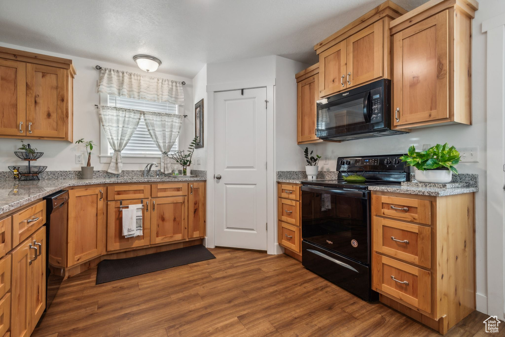 Kitchen featuring sink, black appliances, light stone countertops, and dark hardwood / wood-style flooring