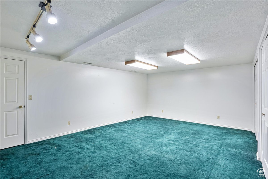Carpeted spare room featuring beam ceiling, track lighting, and a textured ceiling
