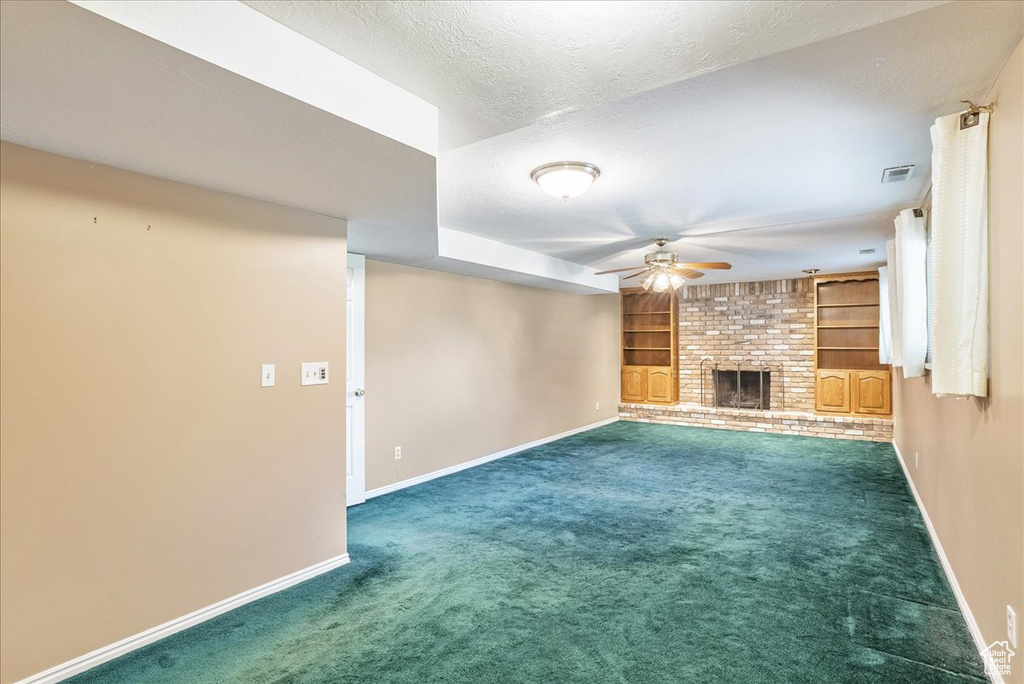 Unfurnished living room featuring a textured ceiling, a brick fireplace, ceiling fan, carpet, and built in shelves