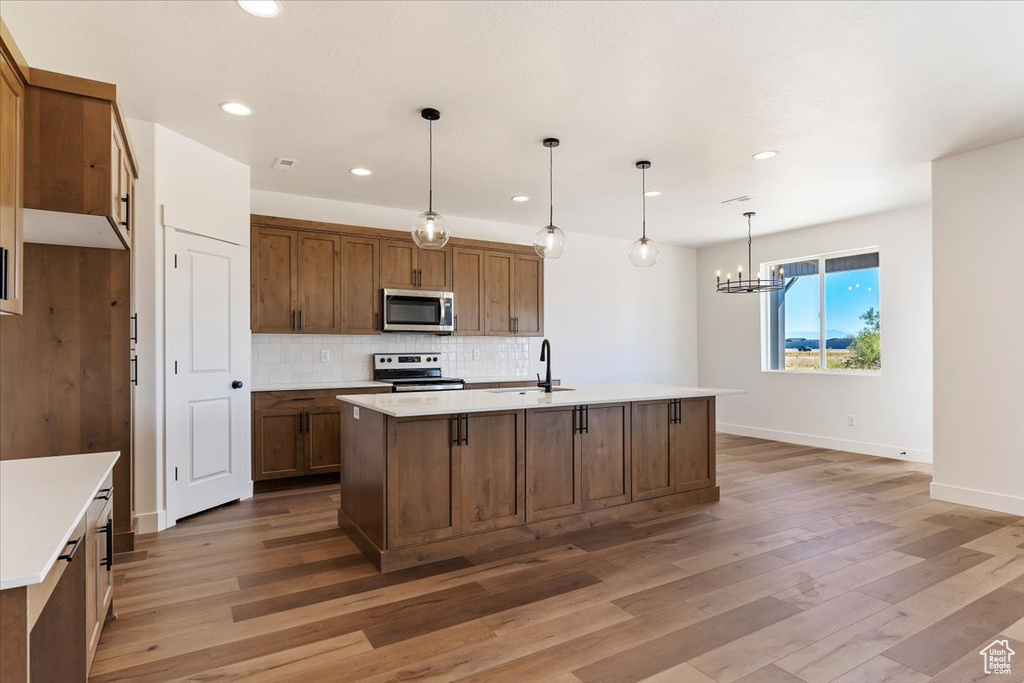 Kitchen with hardwood / wood-style floors, appliances with stainless steel finishes, a kitchen island with sink, sink, and decorative light fixtures