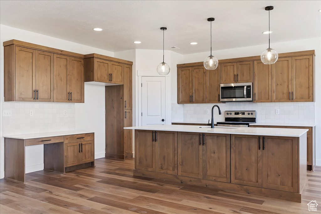 Kitchen featuring dark wood-type flooring, backsplash, appliances with stainless steel finishes, and a kitchen island with sink