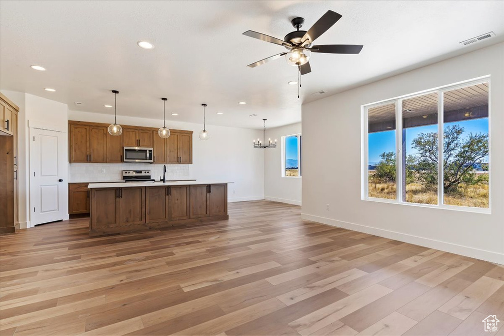 Kitchen featuring sink, light hardwood / wood-style floors, stainless steel appliances, pendant lighting, and a kitchen island with sink