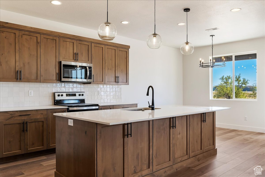 Kitchen with hardwood / wood-style floors, sink, appliances with stainless steel finishes, and hanging light fixtures