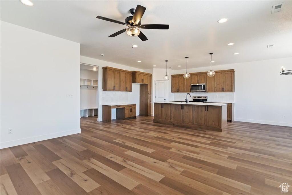 Kitchen with wood-type flooring, ceiling fan, stainless steel appliances, pendant lighting, and a center island with sink