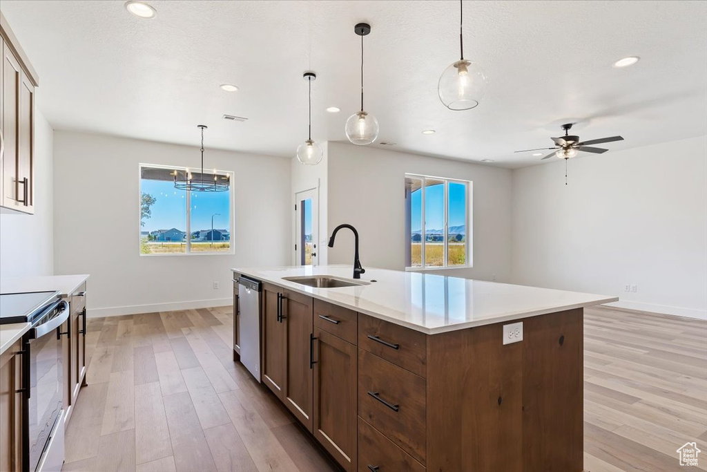 Kitchen featuring sink, light hardwood / wood-style floors, stainless steel dishwasher, range with electric stovetop, and a kitchen island with sink