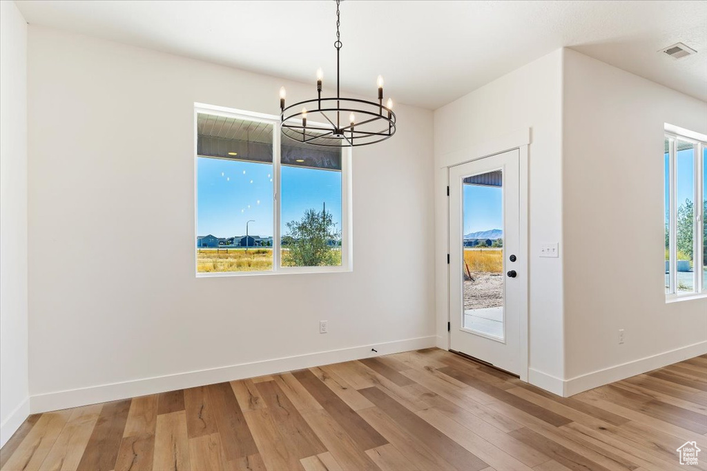 Unfurnished dining area featuring light hardwood / wood-style floors, a healthy amount of sunlight, and an inviting chandelier