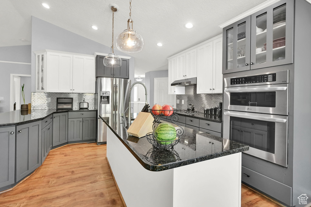 Kitchen with stainless steel appliances, tasteful backsplash, light wood-style flooring, dark stone countertops, and recessed lighting
