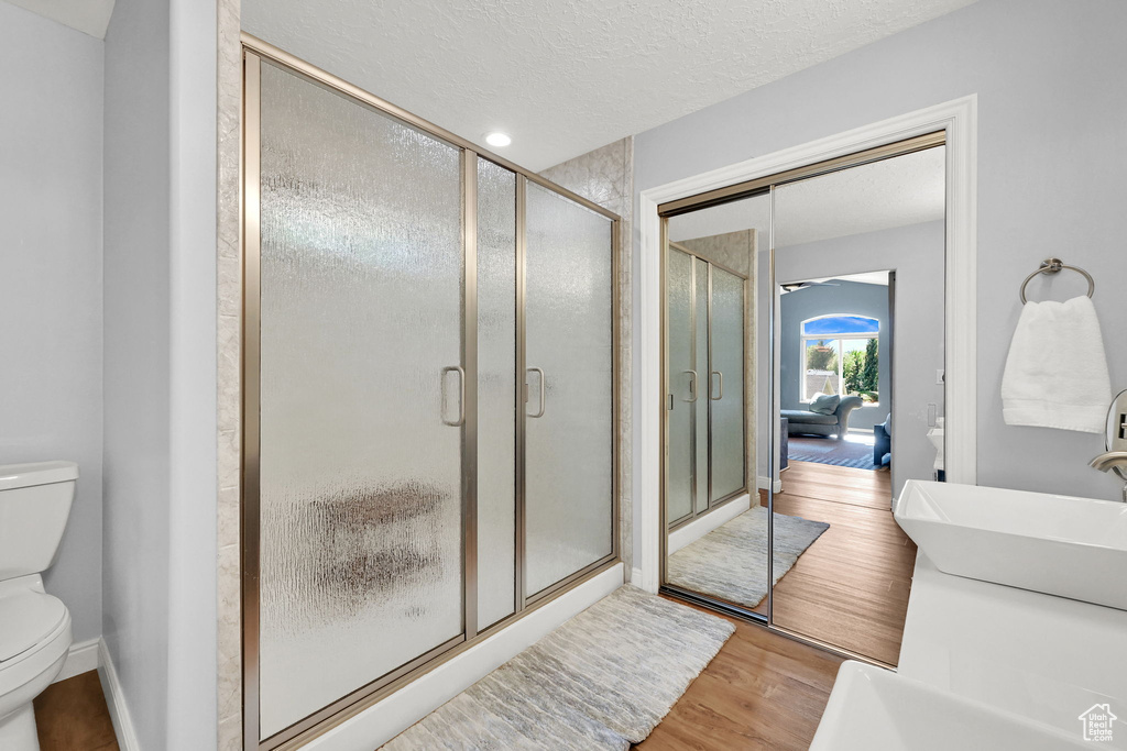 Full bath featuring toilet, wood finished floors, a textured ceiling, a shower stall, and vanity