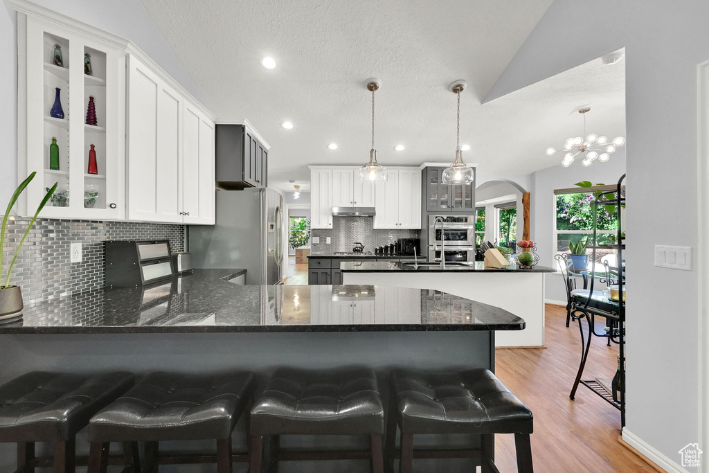 Kitchen with appliances with stainless steel finishes, a peninsula, tasteful backsplash, light wood-style floors, and glass insert cabinets