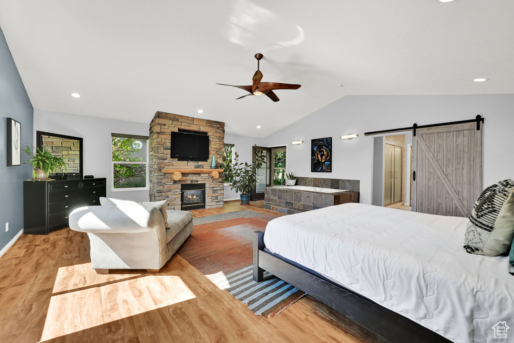 Bedroom with a barn door, vaulted ceiling, light wood finished floors, baseboards, and a fireplace