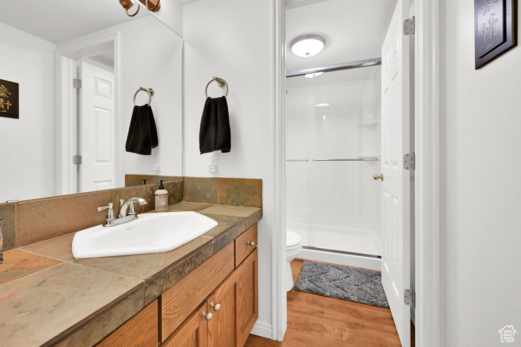 Bathroom featuring toilet, a stall shower, vanity, and wood finished floors