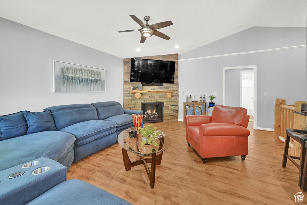 Living room with vaulted ceiling, ceiling fan, light wood-style flooring, a stone fireplace, and recessed lighting