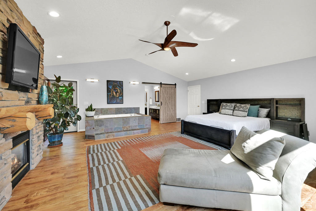 Bedroom with a barn door, lofted ceiling, a large fireplace, light wood finished floors, and ceiling fan