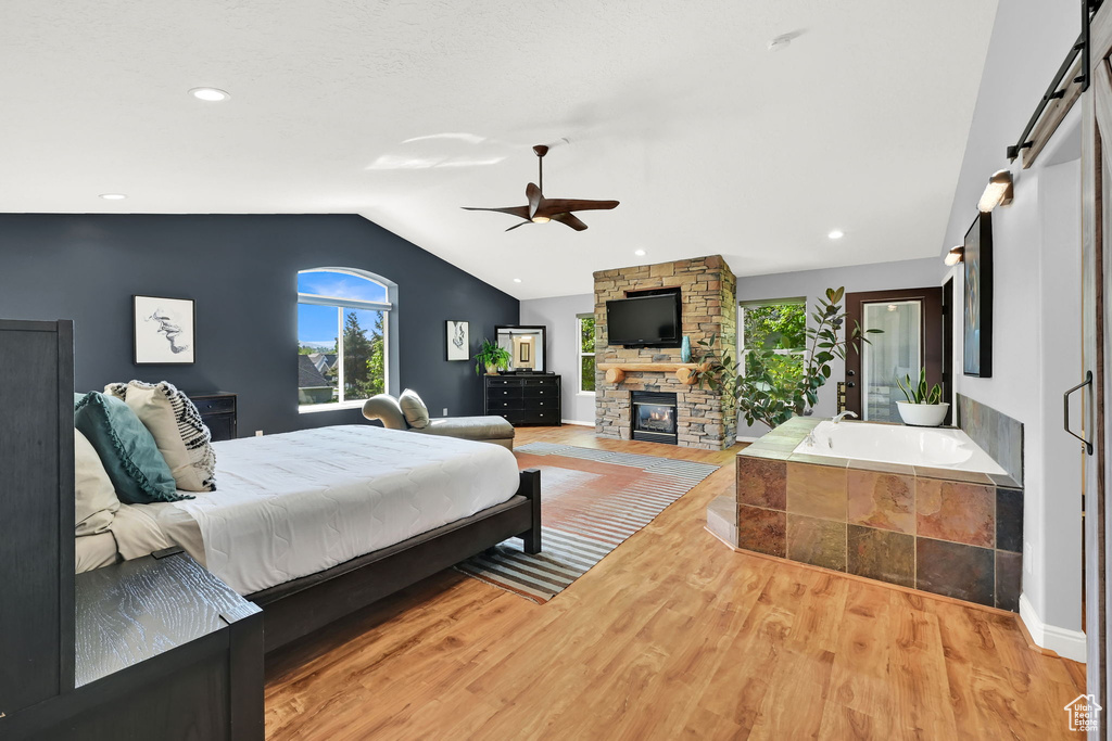 Bedroom with vaulted ceiling, multiple windows, wood finished floors, a fireplace, and ceiling fan