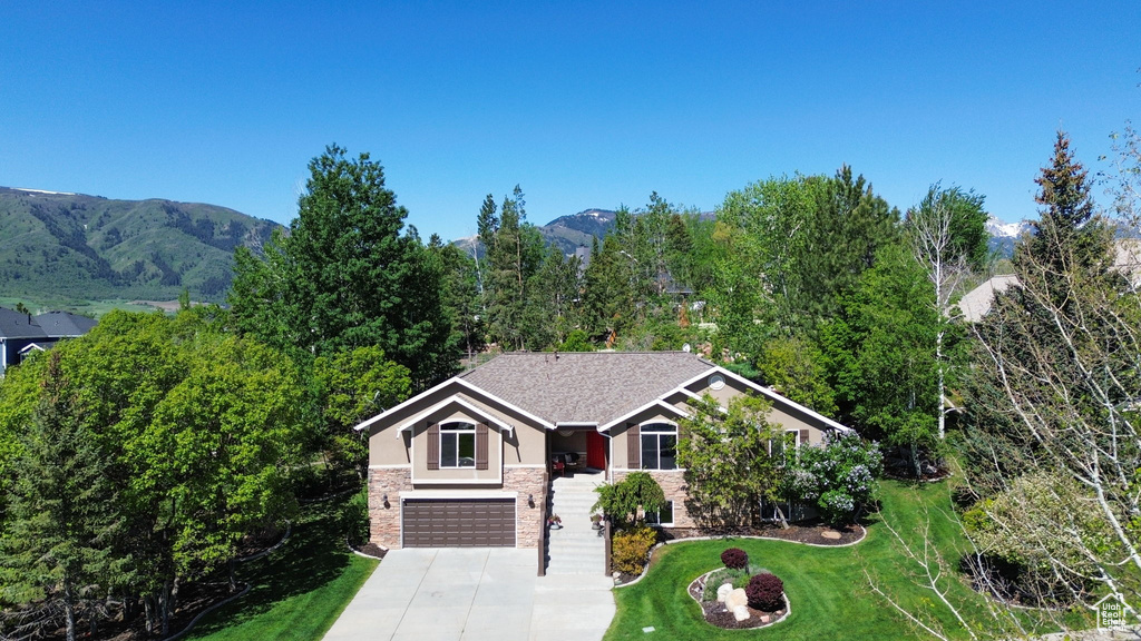View of front of property with an attached garage, a front yard, stucco siding, stone siding, and driveway