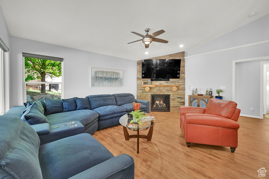 Living area featuring lofted ceiling, ceiling fan, light wood finished floors, and a stone fireplace