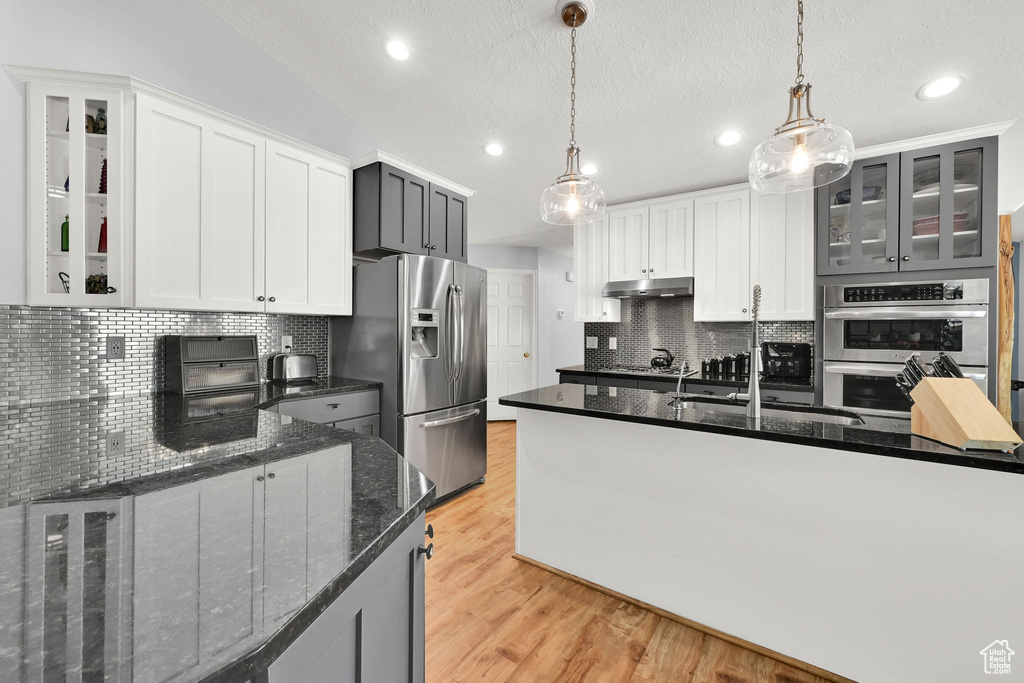 Kitchen with appliances with stainless steel finishes, backsplash, recessed lighting, a sink, and light wood-type flooring