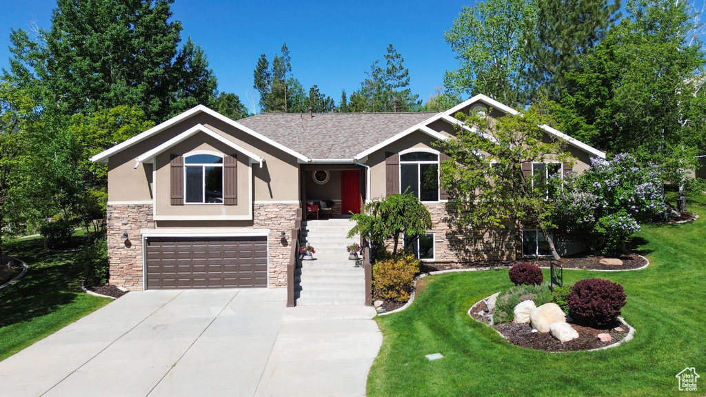 View of front of home featuring stone siding, stucco siding, driveway, a garage, and a front lawn