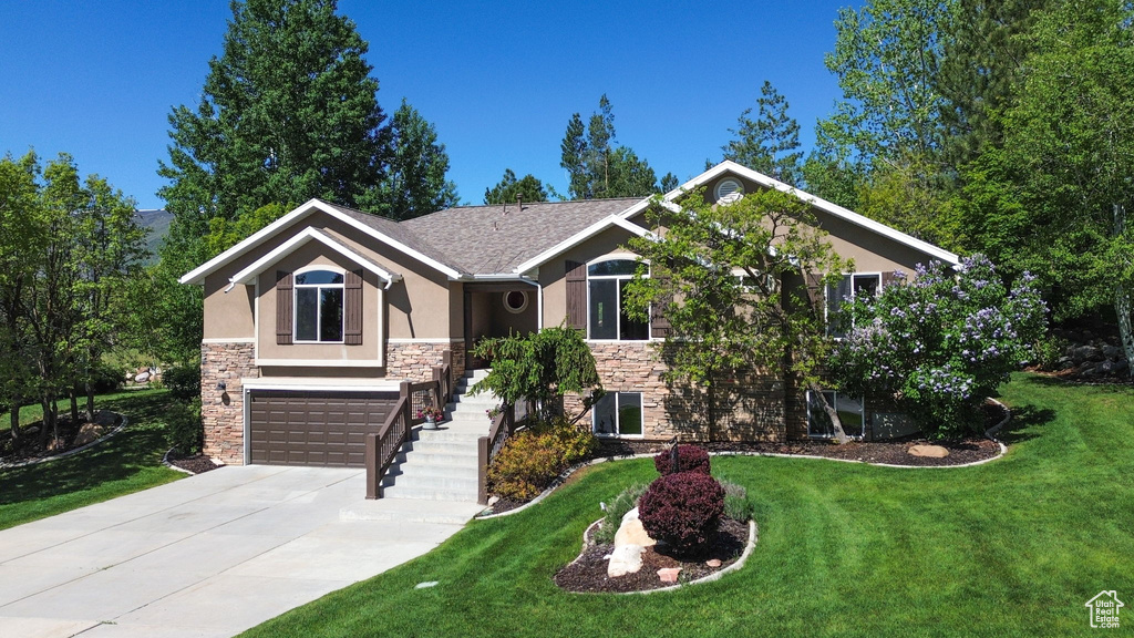 View of front facade featuring stone siding, stucco siding, a front yard, concrete driveway, and an attached garage
