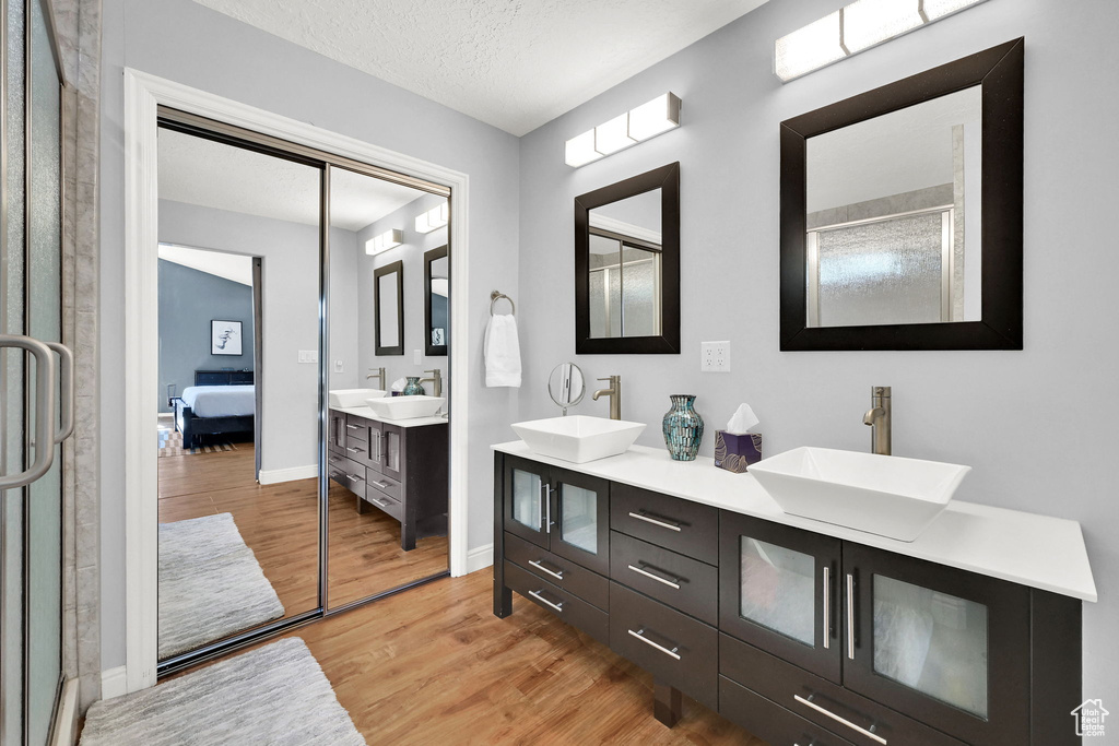Ensuite bathroom with wood finished floors, double vanity, baseboards, and a textured ceiling