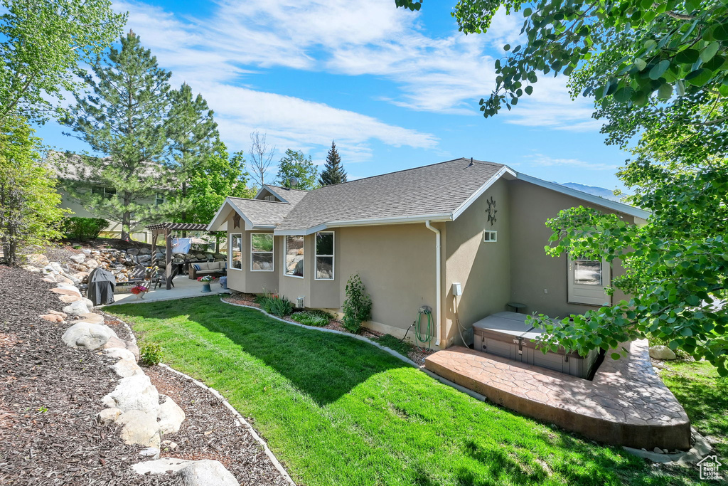 Back of house with stucco siding, a patio area, a yard, and a shingled roof