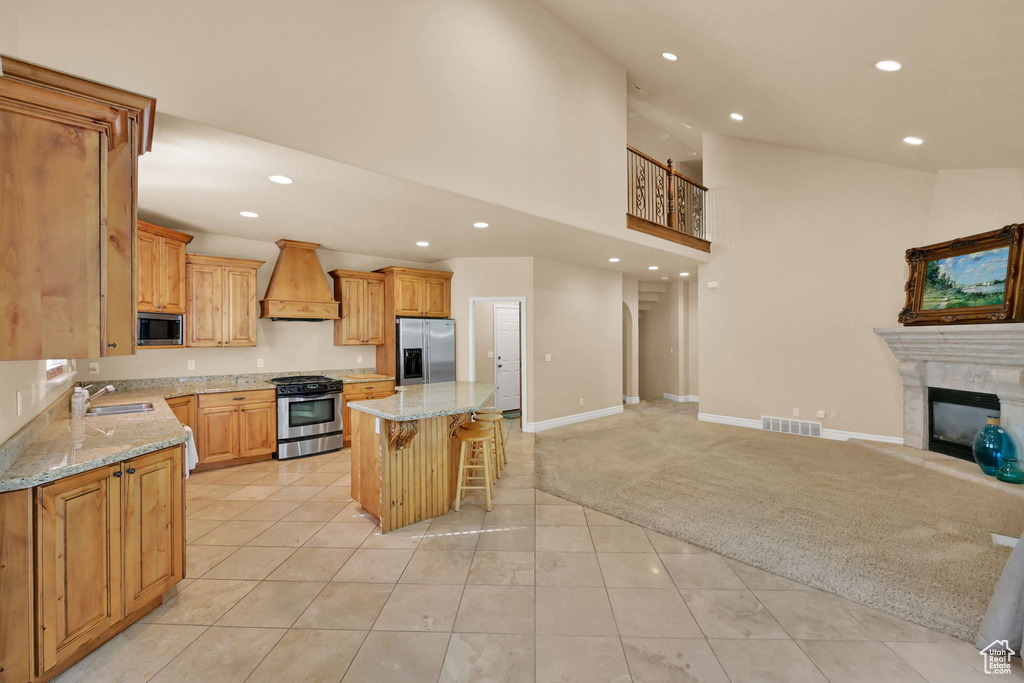 Kitchen with custom exhaust hood, light carpet, a kitchen island, a kitchen breakfast bar, and stainless steel appliances